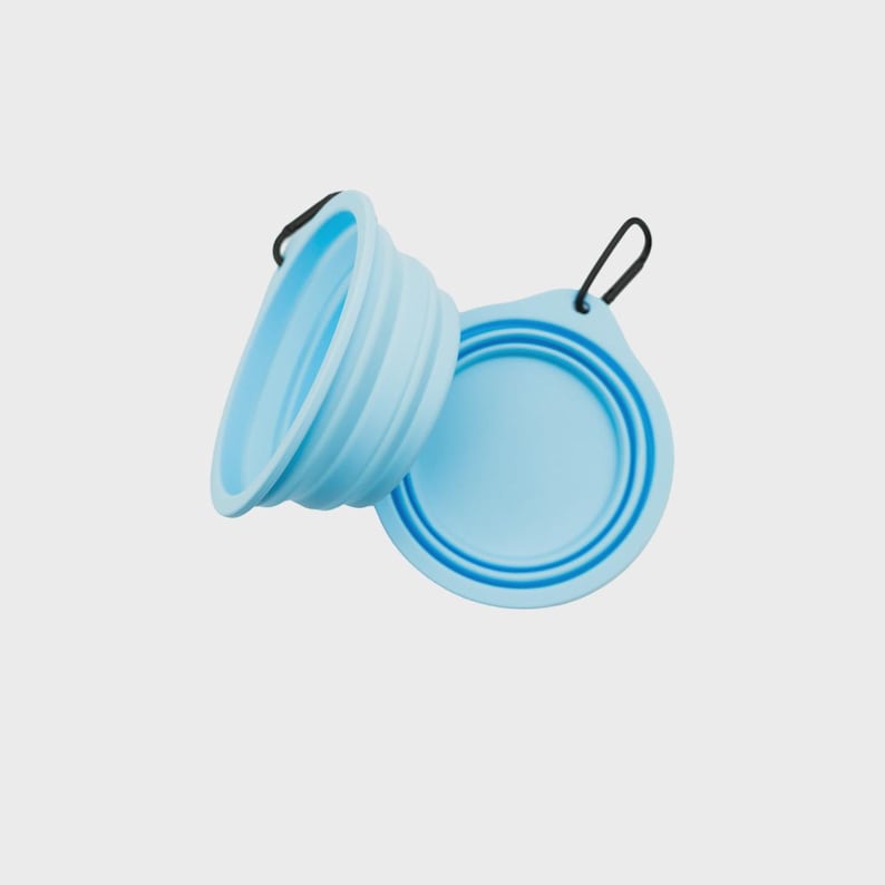 May include: Two light blue collapsible silicone bowls, one shown in a folded flat position and the other in an expanded state. Each bowl features a black metal carabiner attached to a small tab on the rim for easy carrying and attachment.