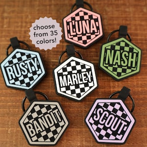 May include: Hexagon-shaped pet tags with names like "Rusty," "Luna," and "Nash" in bold, white lettering. Each tag features a checkered pattern and a black rubber loop. The image also includes a text bubble that says "choose from 35 colors!"