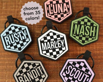 May include: Hexagon-shaped pet tags with names like "Rusty," "Luna," and "Nash" in bold, white lettering. Each tag features a checkered pattern and a black rubber loop. The image also includes a text bubble that says "choose from 35 colors!"