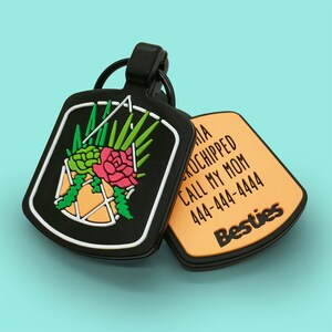 May include: Black pet tag with a floral design in a geometric shape. The tag has a white border and a black ring. The second tag is orange with the text "Besties" and contact information.
