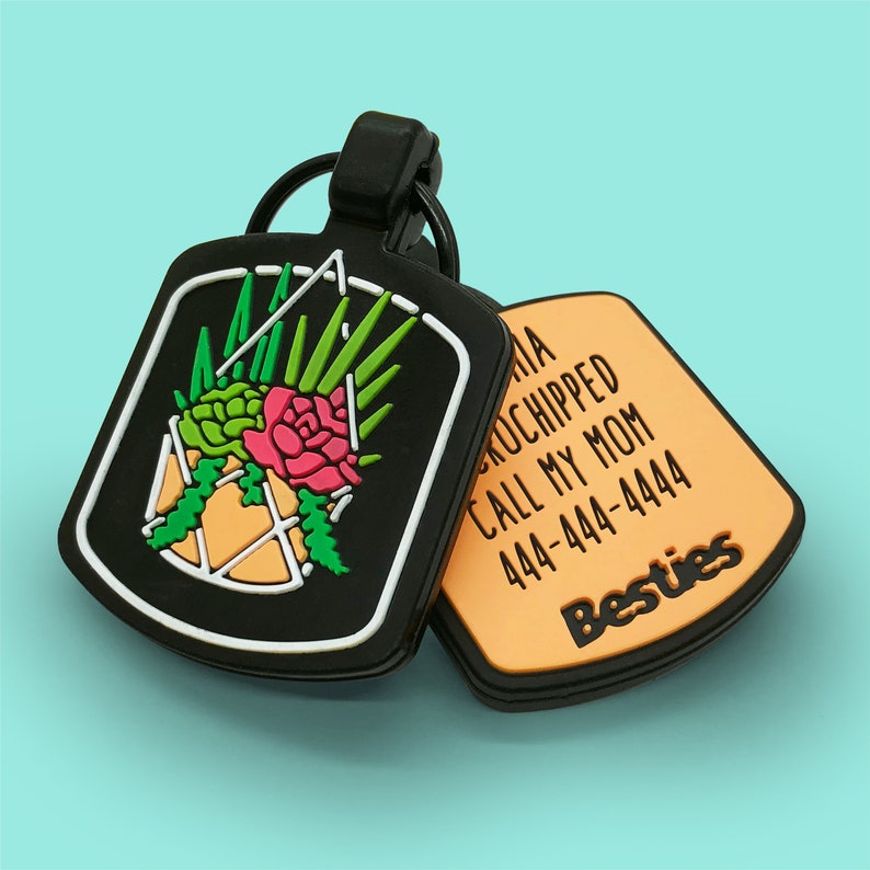 May include: Black pet tag with a floral design in a geometric shape. The tag has a white border and a black ring. The second tag is orange with the text "Besties" and contact information.