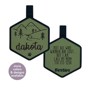 May include: Two green hexagonal dog tags with black trim. The first tag has a mountain scene with a river and the text "dakota". The second tag has the text "NOT ALL WHO WANDER ARE LOST... BUT I AM. CALL MY MOM! 714 777-1234" and the word "Besties".