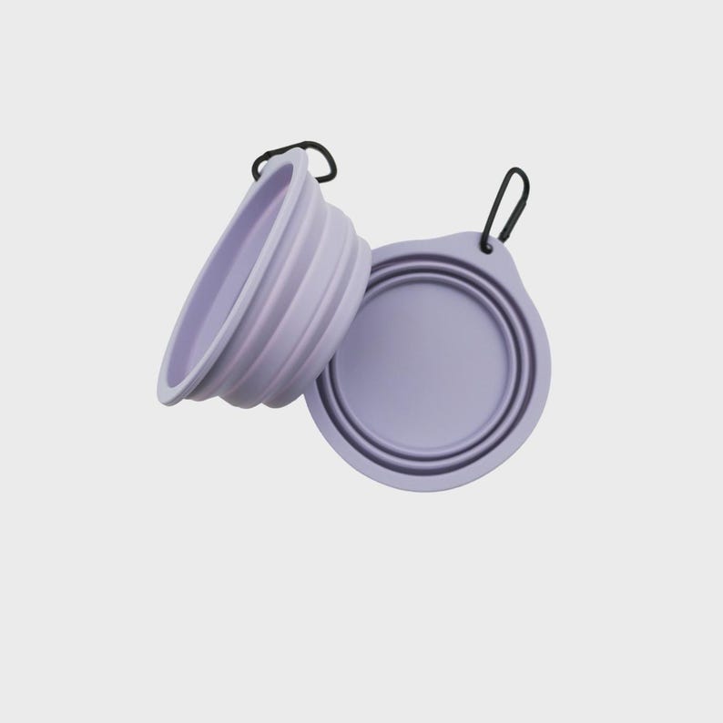 May include: Two light purple collapsible bowls made of flexible silicone. Each bowl features a circular design with concentric ridges for folding and a black metal carabiner attached to a small tab on the rim for easy carrying and attachment.