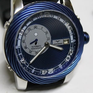 Puede incluir: Primer plano de un reloj de pulsera con un diseño espiral azul en el bisel y la esfera. El reloj tiene una caja plateada y una correa de cuero negro. La esfera tiene números y agujas blancas, con el texto "AUTOMATIC MADE IN RUSSIA".