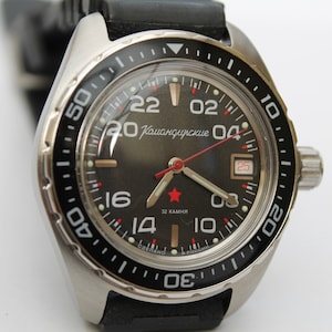 May include: A black and silver wristwatch with a black rubber strap. The watch face has white numbers and a red second hand. The watch face also has the text "Командирские" in Cyrillic script.