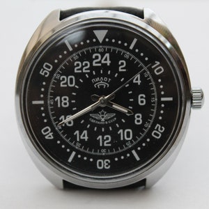 Peut inclure: Une montre-bracelet à cadran noir avec un boîtier argenté et un bracelet en cuir noir. Le cadran de la montre comporte des marques blanches et les mots "Пилот" et "СДЕЛАНО В СССР".