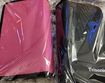 May include: Two zippered cases, one pink and one black, with the word "Trisonix" printed on the black case.
