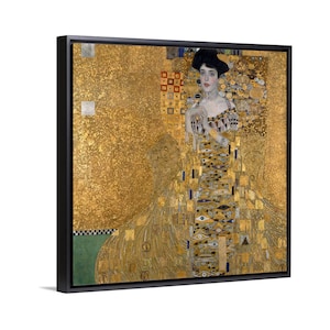 May include: Framed art print of a woman in a gold dress, a famous painting by Gustav Klimt. The artwork features a gold background with intricate patterns and details. The woman is depicted with a serene expression, wearing a dark hat.