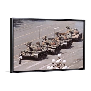 Puede incluir: Impresión enmarcada de una fotografía histórica que representa una fila de tanques militares en una calle de la ciudad. Los tanques son de color verde oliva y marrón, con una persona de pie delante. La imagen está enmarcada en negro.