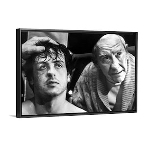 Può includere: Stampa incorniciata in bianco e nero con una scena di un film di boxe. Un pugile sudato guarda in alto, con un uomo anziano preoccupato in accappatoio che osserva. Una mano è appoggiata sulla testa del pugile. L'immagine è un primo piano.