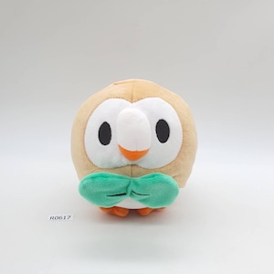 May include: A soft owl plush toy with a round body, tan feathers, and large black eyes. It has a white face, an orange beak, and a green bow tie. The toy is designed for children.