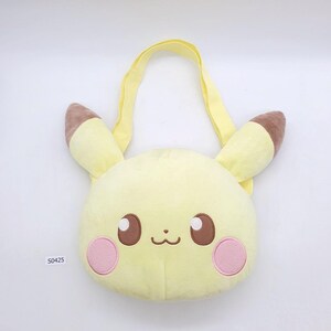 May include: A yellow plush bag shaped like Pikachu's face, featuring brown ears, eyes, and a small mouth. Pink circles represent cheeks. The bag has a yellow handle and is made of soft material. The product code "S0425" is visible.
