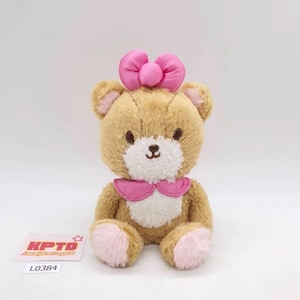 May include: A plush teddy bear with a light brown body, pink bow, and pink accents on the ears, paws, and collar. The bear has a white muzzle and a small, embroidered black nose. A tag with the text "KPTD" and the number "L0384" is visible.