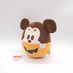 K&ouml;nnte beinhalten: Ein rundes Pl&uuml;schtier mit einem braunen Mickey-Maus-Kopf mit gestickten Gesichtsdetails und Wimpern, das auf einer orangefarbenen, k&uuml;rbisf&ouml;rmigen Basis mit einem schwarzen K&uuml;rbisgesicht sitzt. Ein kleines wei&szlig;es Etikett mit KPTD und A0504 ist sichtbar.