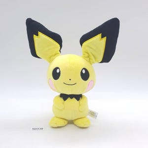 May include: A plush yellow character with large black-tipped ears, pink cheeks, and a black collar. The stuffed animal has a smiling face and small black eyes. The tag reads "S0338".