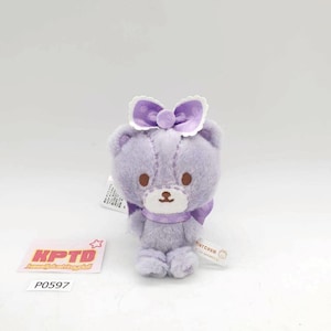 May include: A small, lavender plush bear with a purple bow on its head and a matching scarf. The bear has brown eyes and a stitched design. A tag with the text "TINY CHUM" is attached.