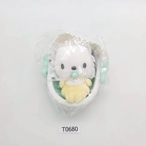 May include: A plush toy of a white puppy with a pacifier, wearing a yellow outfit, inside a white cradle with mint green handles. The toy is wrapped in clear plastic. The text "T0680" is visible.