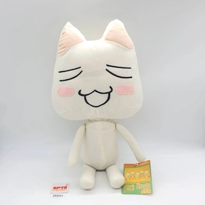 Pode incluir: Um peluche de cor creme com uma cabeça grande e quadrada, orelhas pontiagudas, olhos fechados e um sorriso largo e aberto. A personagem tem bochechas cor-de-rosa suaves e braços e pernas finos e pendentes. Uma pequena etiqueta está anexada.