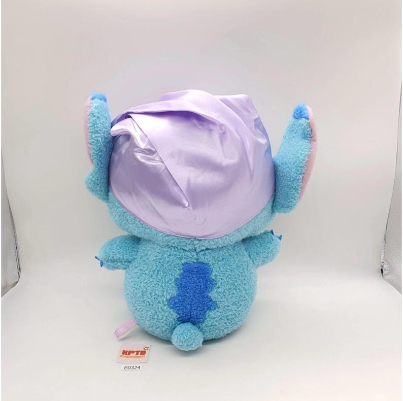 May include: A plush toy of a blue alien-like creature with large ears and a small tail. The toy is wearing a lavender satin bonnet. The toy has a tag with the text "KPTB" and the number "E0324".