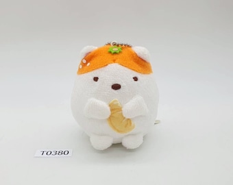 May include: A plush white and orange hamster-like character with a small croissant. The stuffed animal has a small metal chain and a flower on its head. The text "T0380" is printed on a white label.