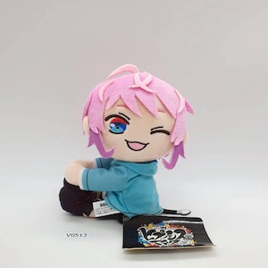 May include: A plush doll with pink hair and blue eyes, dressed in a blue hoodie and black trousers. The doll is winking and smiling. A black tag with Japanese text is attached. The product code "V0513" is visible.