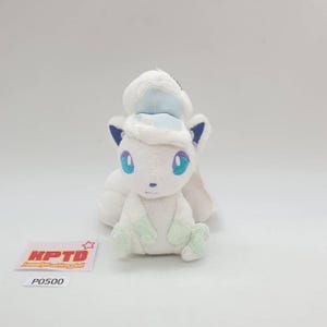 May include: A white plush fox toy with blue eyes, ears, and details, wearing a light blue hat. The fox has light green paws and a fluffy tail. A tag with the text "KPTD" and "P0500" is visible.