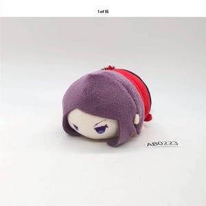 May include: A plush doll with a purple head, red and black accents, and a white face with blue eyes. The doll has a small metal loop at the top. The tag reads "AB0223".