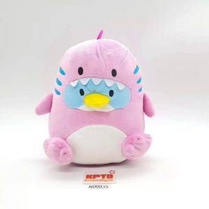 May include: A pink plush toy shaped like a penguin with blue accents and a yellow beak. The toy has a white belly and small arms and feet. The toy has the text "KPTD" and "N00035" on a small white rectangle.