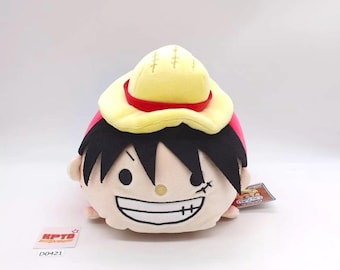 May include: A plush toy of a character with black hair, a yellow hat with a red band, and a stitched scar under the eye. The toy has a wide, toothy grin and a small tag. The text "KPTD" and "D0421" are visible.