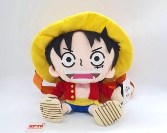 May include: A plush toy of a cartoon character with black hair, a yellow hat, and a red jacket. The toy has a smiling expression and is wearing blue shorts. The toy is sitting with its legs extended and has tan shoes. The tag reads "KPTD E0322".