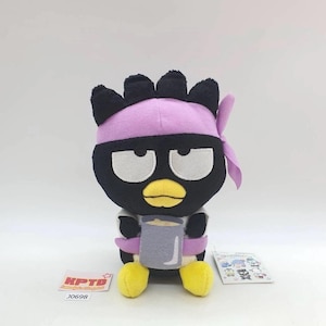 May include: A plush toy of a black penguin-like character with a purple headband, holding a gray mug. The toy has white eyes, a yellow beak, and yellow feet. The tag reads "KPTD" and "J0698".
