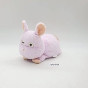 Puede incluir: Un peluche de conejo lavanda con el interior de las orejas y las patas de color rosa claro. El conejo tiene ojos grandes y redondos y una pequeña nariz rosa. El juguete está tumbado sobre una superficie blanca. La etiqueta dice "T0401".