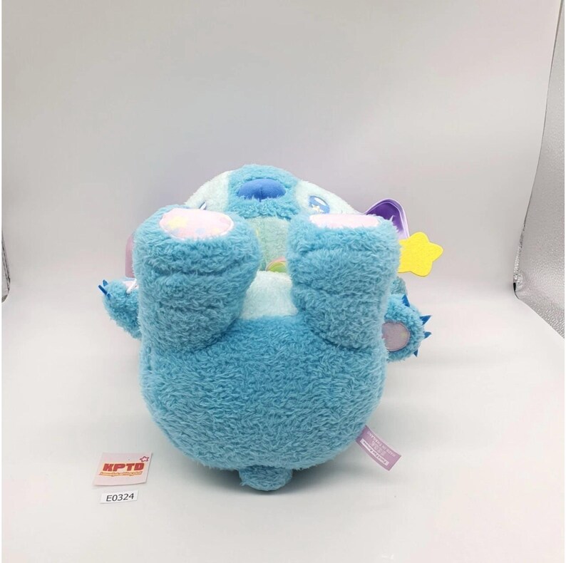 May include: A plush toy in a light blue color, with a round body and large, fluffy feet. The toy has a light blue head with a dark blue patch and a yellow star. The toy has a tag that says "KPTD" and "E0324".