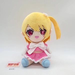 May include: A plush doll with yellow hair, large pink eyes with star accents, and a small smile. The doll wears a pink dress with a white bow at the chest, white gloves, and light blue shoes. A small white card with the text KPTD 10448 is visible.
