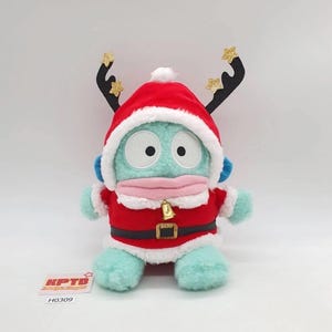 May include: A plush toy in a Santa Claus outfit with reindeer antlers. The toy is light blue with large eyes and a pink mouth. The Santa suit is red with white trim and a gold belt. The antlers are black with gold star accents.