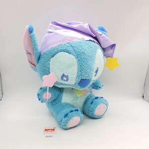 May include: A plush Stitch toy in a seated position, featuring a light blue body, large ears, and a lavender nightcap. The toy holds a pink star wand and has yellow star accents. The toy has a tag that reads "KPTB" and "E0324".