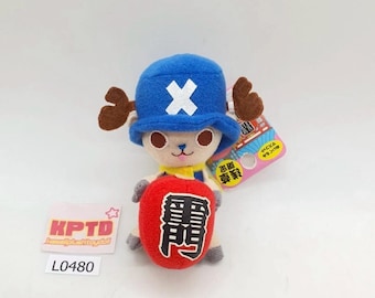 May include: A plush toy of Tony Tony Chopper from the anime One Piece. Chopper is wearing a blue hat with a white X on it and holding a red Japanese lucky charm with the kanji for "victory" on it.