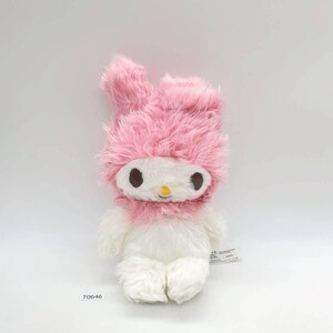 May include: A soft toy with a pink, fluffy bunny-eared hat and collar, and a white face and body. The toy has brown eyes and a yellow nose. The tag reads "T0646".