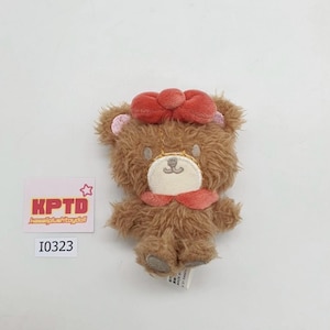 May include: A small, brown plush bear with a red bow on its head and a matching scarf. The bear has a white face and embroidered details. The tag reads "KPTD" and "I0323".