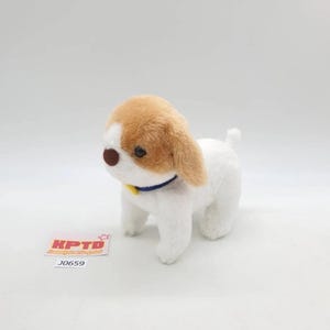 Puede incluir: Un perro de peluche con pelaje blanco y orejas y cabeza marrones. Tiene un collar azul y una etiqueta amarilla. El juguete está sobre una superficie blanca.