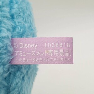 May include: A close-up of a light blue plush toy with a lavender tag. The tag features the Disney logo, the number 1038818, and Japanese text. The plush toy is partially visible.