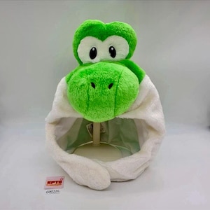 Peut inclure: Un chapeau en peluche représentant une tête de dinosaure vert vif avec de grands patchs oculaires blancs et des pupilles noires. Le chapeau présente une texture douce en polaire blanche autour du visage et deux longs rabats blancs latéraux.