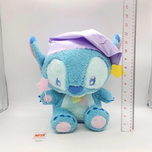 May include: A plush blue Stitch toy wearing a lavender nightcap and holding a pink star wand. The toy has yellow star accents and is approximately 10 inches tall, with a ruler in the background.