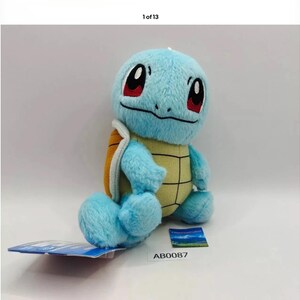 May include: A plush Squirtle toy in light blue, with a yellow and brown shell, red eyes, and black accents. The toy is sitting on a white surface with a tag attached. The tag has the number AB0087.