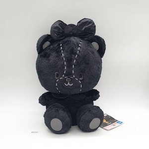 May include: A plush black teddy bear with a large bow on its head. The bear has gray accents on its ears, paws, and face, with stitched details. It has a small collar and is sitting upright. A tag is visible on the right side.