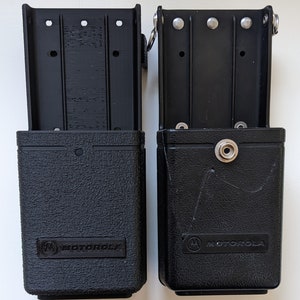 May include: Two black Motorola radio holsters with a textured finish and the Motorola logo. The holsters have a clip on the top and a snap closure on the front.