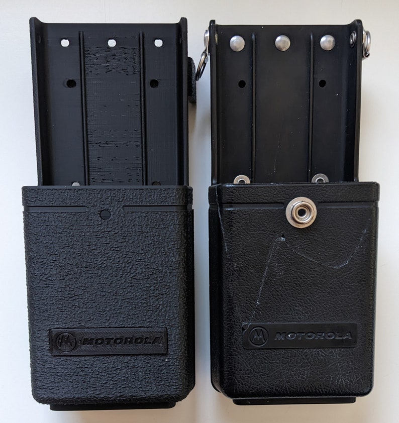 May include: Two black Motorola radio holsters with a textured finish and the Motorola logo. The holsters have a clip on the top and a snap closure on the front.