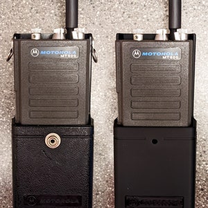 May include: Two black Motorola MT 600 two-way radios in black holsters. The radios have a black antenna and silver buttons.