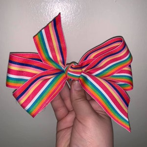 May include: A colorful rainbow striped bow made from ribbon. The bow is tied in a classic shape with the ends of the ribbon forming points.