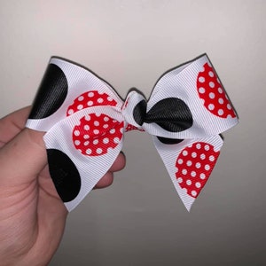 May include: A white bow with red and black polka dots. The bow is tied in a knot and has a white ribbon.
